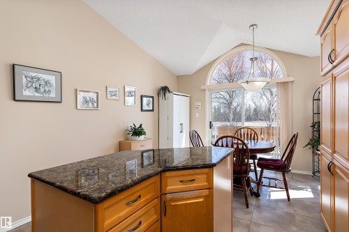 The kitchen features a functional island with a dark countertop and light wood cabinetry, complemented by a vaulted ceiling - 14 920 119 Street, Edmonton, AB - Indoor