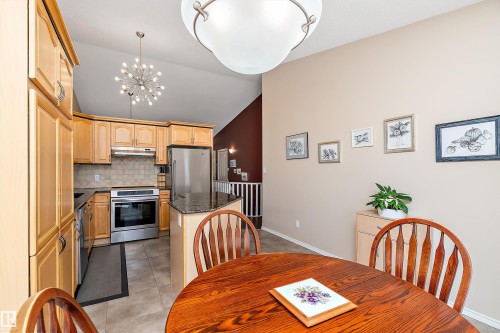 Well-appointed kitchen featuring light wood cabinetry, stainless steel appliances, and a granite-topped island with seating - 14 920 119 Street, Edmonton, AB - Indoor