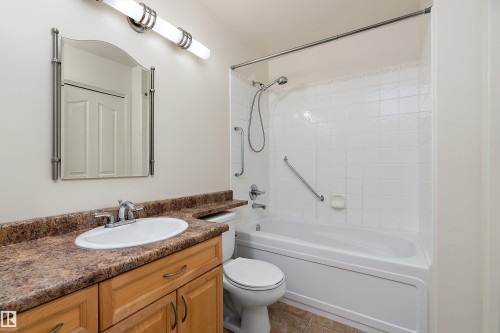 The bathroom features a vanity with a brown countertop and a white oval sink, a mirror with a brushed nickel frame, and a bathtub with white tiled walls and a shower head - 14 920 119 Street, Edmonton, AB - Indoor Photo Showing Bathroom