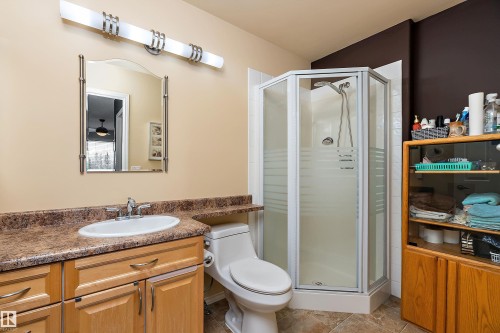 Bathroom featuring a corner shower with a glass enclosure, a vanity with a light-toned countertop and wood cabinetry, and a wall-mounted mirror with an overhead light fixture - 14 920 119 Street, Edmonton, AB - Indoor Photo Showing Bathroom
