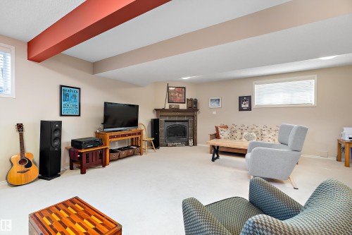 This spacious room features neutral-toned walls, light-colored carpeting, and a fireplace with a dark wood mantel - 14 920 119 Street, Edmonton, AB - Indoor With Fireplace