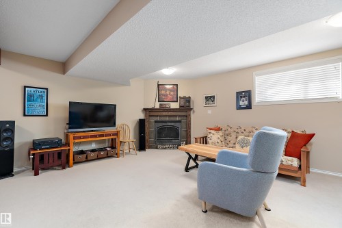This room features light-colored walls, carpeted flooring, and a fireplace with a stone surround - 14 920 119 Street, Edmonton, AB - Indoor With Fireplace