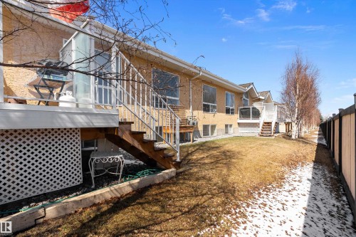 The property features a private deck with wooden stairs leading to the yard, which includes a lawn and mature trees, all enclosed by a fence - 14 920 119 Street, Edmonton, AB - Outdoor