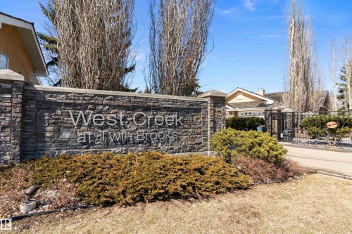 Community entrance featuring a stone wall with "West Creek at Twin Brooks" signage, surrounded by landscaping, and an entry gate - 14 920 119 Street, Edmonton, AB - Outdoor