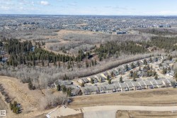 Aerial view showcasing the residential community, characterized by rows of properties with pitched roofs, and surrounded by extensive natural landscapes including forests and open fields - 