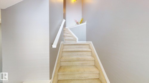 Staircase with carpeted steps and a white handrail, featuring light-colored walls - 5929 8 Avenue, Edmonton, AB - Indoor Photo Showing Other Room