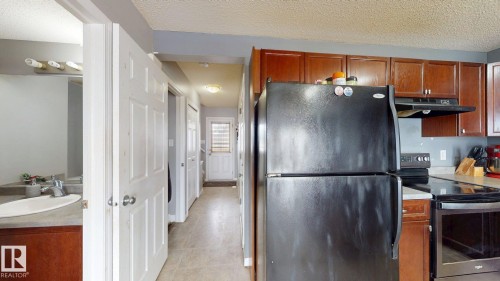 The property features a kitchen with dark cabinetry and black appliances, including a refrigerator and stove - 5929 8 Avenue, Edmonton, AB - Indoor Photo Showing Kitchen