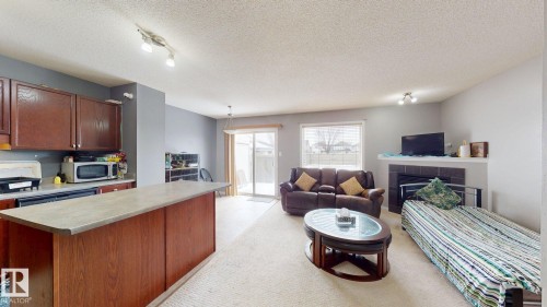 Open concept living area featuring a kitchen island with a stone-look countertop, dark wood cabinetry, a fireplace with a mantel, and a sliding glass door providing access to the exterior - 5929 8 Avenue, Edmonton, AB - Indoor