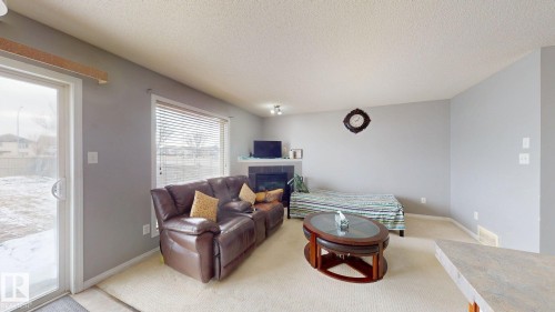 Bright living area featuring a fireplace, a large window with blinds, and a sliding glass door leading to the yard - 5929 8 Avenue, Edmonton, AB - Indoor Photo Showing Living Room