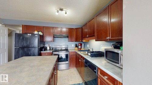 The kitchen features wood cabinetry, a central island with a light-colored countertop, and recessed lighting - 5929 8 Avenue, Edmonton, AB - Indoor Photo Showing Kitchen