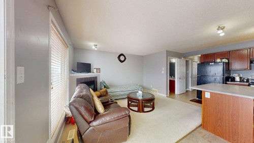 Living room featuring light-colored carpet, a corner fireplace, and large windows with horizontal blinds - 5929 8 Avenue, Edmonton, AB - Indoor Photo Showing Other Room With Fireplace