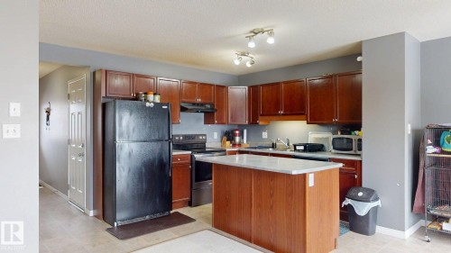 The kitchen features dark wood cabinetry, a central island with a light-colored countertop, and a full suite of black appliances - 5929 8 Avenue, Edmonton, AB - Indoor Photo Showing Kitchen