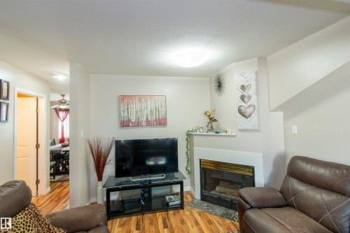 Living area featuring hardwood flooring, a corner fireplace with a mantel, and light-colored walls - 2 9703 174 Street, Edmonton, AB - Indoor Photo Showing Living Room With Fireplace