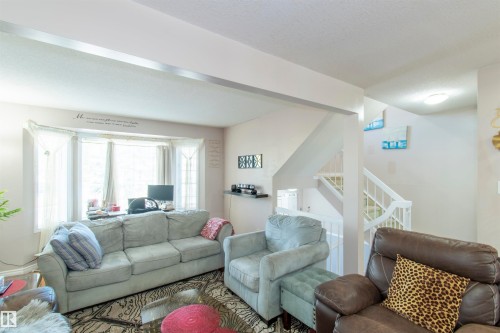 This living area features a bay window providing natural light, a staircase with white railings, and light-colored walls - 2 9703 174 Street, Edmonton, AB - Indoor Photo Showing Living Room