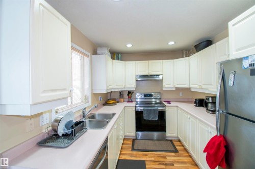 The kitchen features white cabinetry, a double basin sink, stainless steel appliances, and wood-look flooring - 2 9703 174 Street, Edmonton, AB - Indoor Photo Showing Kitchen With Double Sink