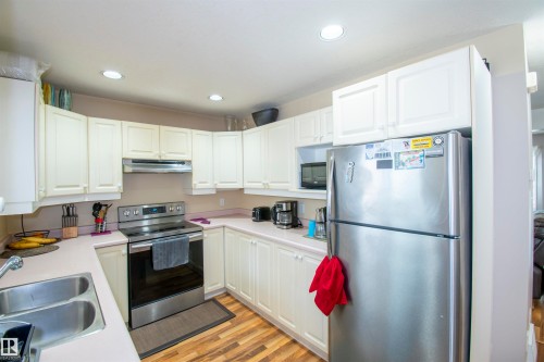 The kitchen features white cabinetry, a double basin sink, stainless steel appliances including a refrigerator and range, and recessed lighting - 2 9703 174 Street, Edmonton, AB - Indoor Photo Showing Kitchen With Double Sink