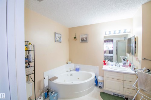 The bathroom features a corner-fitted soaking tub, a vanity with a sink, and an overhead mirror with strip lighting - 2 9703 174 Street, Edmonton, AB - Indoor Photo Showing Bathroom