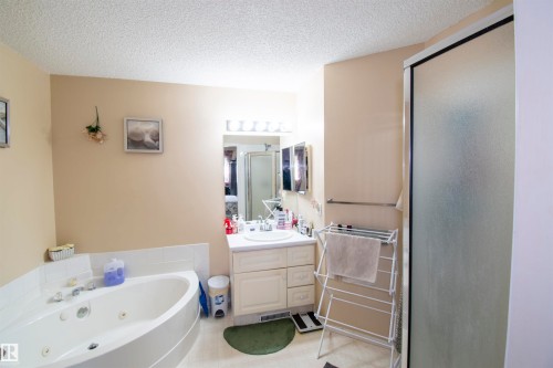 Bathroom featuring a corner bathtub, a single vanity with a mirror and overhead lighting, and a shower with a frosted glass door - 2 9703 174 Street, Edmonton, AB - Indoor Photo Showing Bathroom
