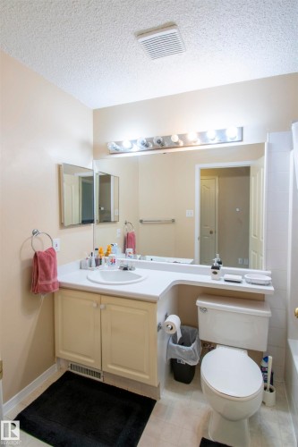 Bathroom featuring a vanity with a white countertop and an integrated sink, a toilet, and a bathtub with white tile surround - 2 9703 174 Street, Edmonton, AB - Indoor Photo Showing Bathroom