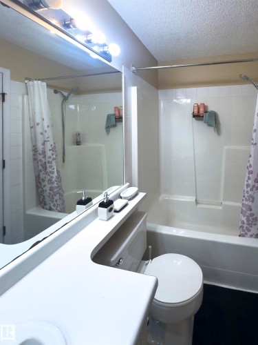 The bathroom features a toilet, a full bathtub with a shower, and a vanity with an integrated sink and mirror - 2 9703 174 Street, Edmonton, AB - Indoor Photo Showing Bathroom