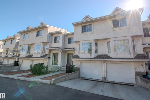 Exterior view of the property featuring a light-colored stucco finish, bay windows, and a two-car garage with white doors - 2 9703 174 Street, Edmonton, AB - Outdoor With Facade