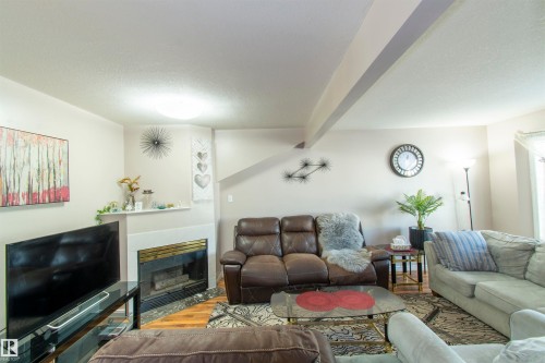 Living room featuring a fireplace with a stone surround, hardwood flooring, and a ceiling light fixture - 2 9703 174 Street, Edmonton, AB - Indoor Photo Showing Living Room With Fireplace