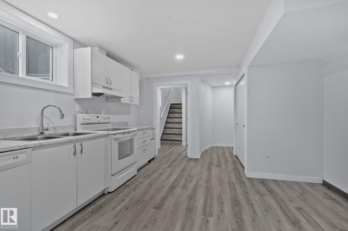 The kitchen features white cabinetry, a double basin sink with a gooseneck faucet, and light-colored countertops - 12002 37 Street, Edmonton, AB - Indoor Photo Showing Kitchen With Double Sink