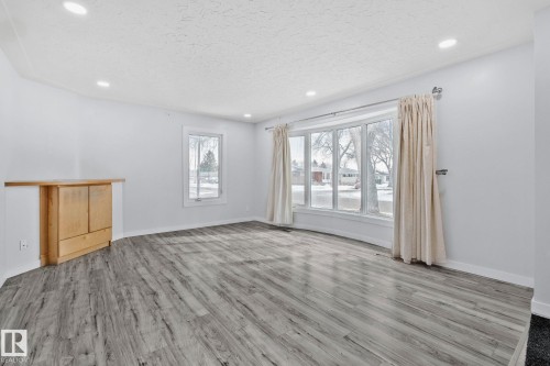 Spacious living area featuring grey wood-look flooring, recessed lighting, and a large bay window - 12002 37 Street, Edmonton, AB - Indoor Photo Showing Other Room