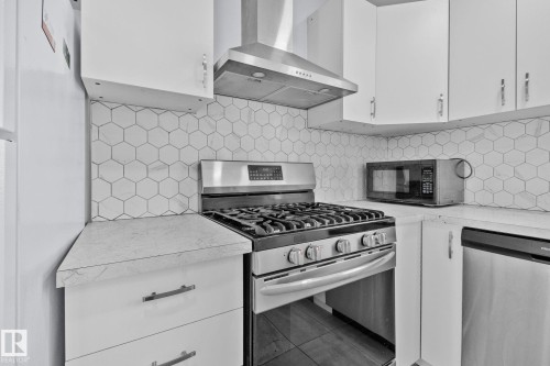 The kitchen features white cabinetry, a hexagonal tiled backsplash, a stainless steel range with a matching range hood, and a built-in dishwasher - 12002 37 Street, Edmonton, AB - Indoor Photo Showing Kitchen