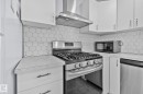 The kitchen features white cabinetry, a hexagonal tiled backsplash, a stainless steel range with a matching range hood, and a built-in dishwasher - 12002 37 Street, Edmonton, AB  - Indoor Photo Showing Kitchen 