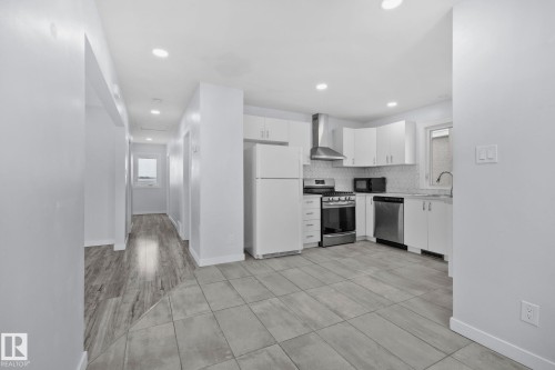 The kitchen features white cabinetry, stainless steel appliances, and tiled flooring - 12002 37 Street, Edmonton, AB - Indoor Photo Showing Kitchen