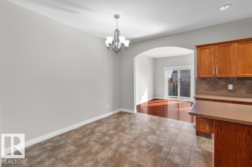 This property features an open layout with tiled flooring, a contemporary chandelier, and an archway leading to a room with hardwood flooring and sliding glass doors - 16419 53 Street, Edmonton, AB - Indoor