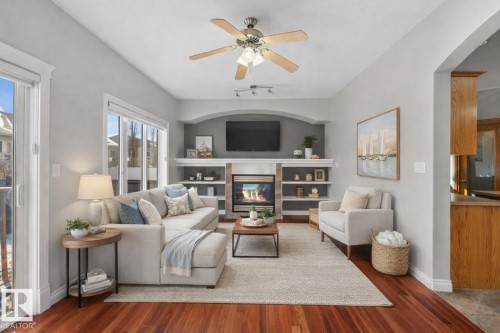 Living area featuring rich hardwood floors, a ceiling fan with integrated lighting, and glass sliding doors providing external views - 16419 53 Street, Edmonton, AB - Indoor Photo Showing Living Room With Fireplace