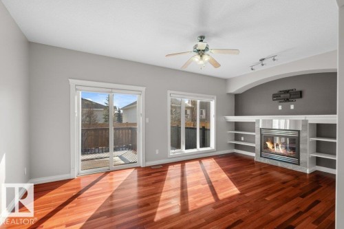 Living area featuring hardwood flooring, a fireplace with a tile surround, built-in shelving, and direct access to an outdoor deck through sliding glass doors - 16419 53 Street, Edmonton, AB - Indoor With Fireplace
