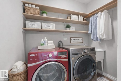 Dedicated laundry area featuring a red front-loading washing machine, a grey front-loading dryer, a utility sink, and wall-mounted shelving for storage - 16419 53 Street, Edmonton, AB - Indoor Photo Showing Laundry Room