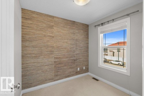 This room features a textured accent wall, light-colored carpeting, and a window with blinds providing natural light - 16419 53 Street, Edmonton, AB - Indoor Photo Showing Other Room