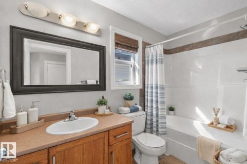 The bathroom features a vanity with a countertop and an integrated sink, a framed mirror, and a window with blinds - 16419 53 Street, Edmonton, AB - Indoor Photo Showing Bathroom