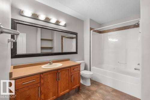 This bathroom features a spacious vanity with wood cabinetry, a large mirror with a dark frame, and a combination bathtub and shower with tiled accents - 16419 53 Street, Edmonton, AB - Indoor Photo Showing Bathroom