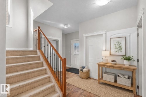 Entryway featuring a carpeted staircase with a wood and wrought iron railing, a front door with decorative glass, and a tiled floor - 16419 53 Street, Edmonton, AB - Indoor Photo Showing Other Room