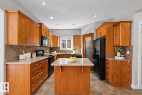The kitchen features extensive wood cabinetry, an island with a countertop, a black refrigerator, and a built-in microwave - 16419 53 Street, Edmonton, AB - Indoor Photo Showing Kitchen