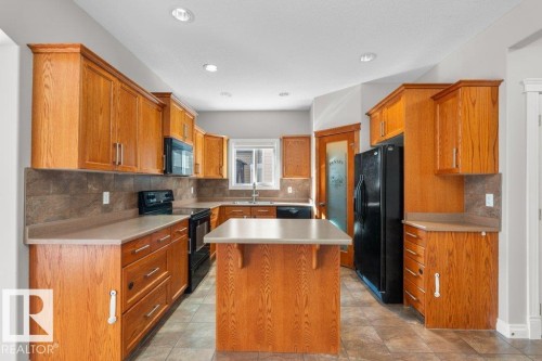 The kitchen features wood cabinetry, a central island, and modern appliances including a black refrigerator, oven, and microwave - 16419 53 Street, Edmonton, AB - Indoor Photo Showing Kitchen With Double Sink