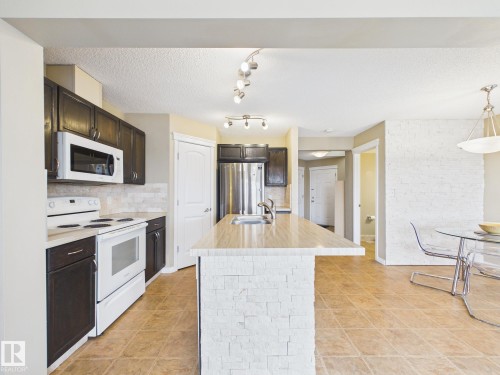 The kitchen features dark wood cabinetry, white appliances, and a central island with a stone-clad base and a light-colored countertop - 9073 Scott Crescent, Edmonton, AB - Indoor Photo Showing Kitchen With Double Sink