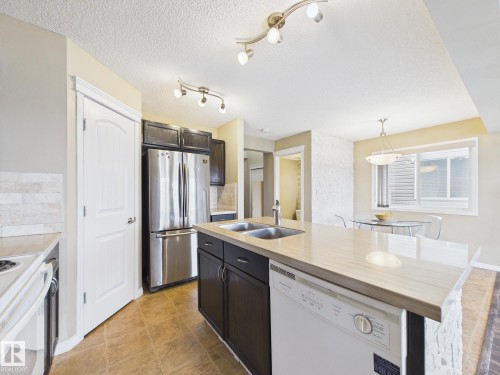 Kitchen featuring stainless steel appliances, dark wood cabinetry, a double basin sink, and a dishwasher integrated into the island - 9073 Scott Crescent, Edmonton, AB - Indoor Photo Showing Kitchen With Double Sink