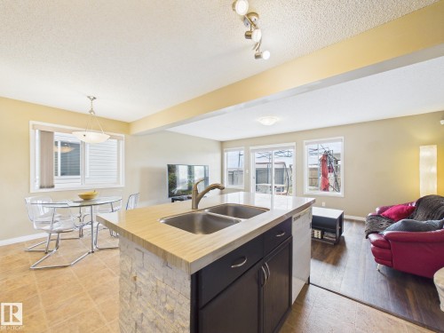 Open concept living area featuring a kitchen island with a double sink, a dining area with a window, and a living room with sliding glass doors leading to the exterior - 9073 Scott Crescent, Edmonton, AB - Indoor