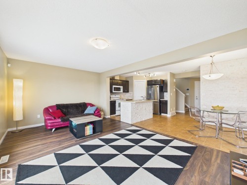 The open-concept living space features dark wood-style flooring and a geometric area rug, with a kitchen area visible in the background - 9073 Scott Crescent, Edmonton, AB - Indoor Photo Showing Other Room