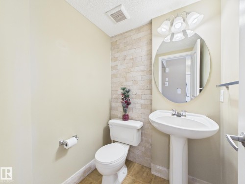 This powder room features a pedestal sink, a toilet, and a tiled accent wall - 9073 Scott Crescent, Edmonton, AB - Indoor Photo Showing Bathroom