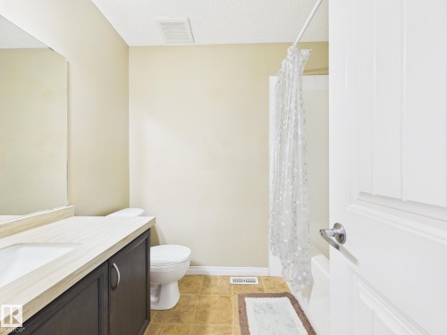 This bathroom features a vanity with a light-colored countertop and a dark-toned cabinet, a toilet, and a shower with a white tub - 9073 Scott Crescent, Edmonton, AB - Indoor Photo Showing Bathroom