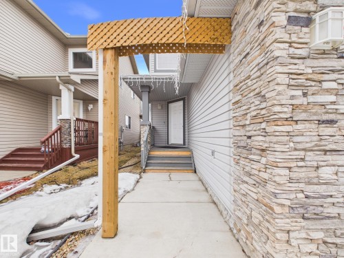 The property features a front entrance with a wooden trellis accent and stone siding, complemented by light-colored horizontal siding - 9073 Scott Crescent, Edmonton, AB - Outdoor