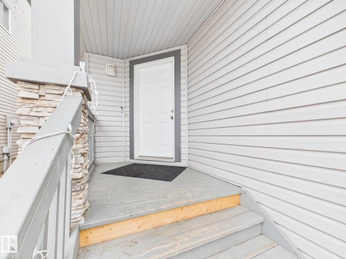 The property features a white paneled entry door with dark trim, light gray siding, and a porch with wood steps and a stone pillar - 9073 Scott Crescent, Edmonton, AB - Outdoor With Exterior