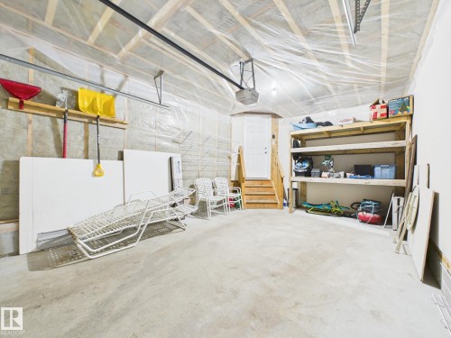 The property includes a spacious garage with a concrete floor, exposed wooden beams, and a white door with wooden stairs - 9073 Scott Crescent, Edmonton, AB - Indoor